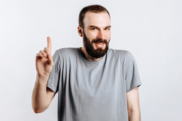 Fototapeta premium Portrait of cheerful young handsome man smiling looking at camera pointing finger upwards on white background with space for advertising mock up