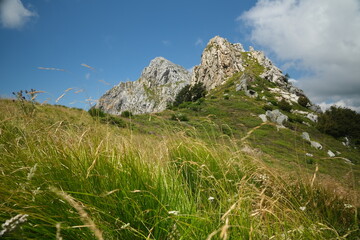 Clouds on top of a mountain in the Apuan Alps in Tuscany.The rock at the top of the mountains contrasts with the green of the meadows and plants. Apuan Alps, Tuscany, Italy. 