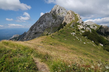 Clouds on top of a mountain in the Apuan Alps in Tuscany.The rock at the top of the mountains contrasts with the green of the meadows and plants. Apuan Alps, Tuscany, Italy. 