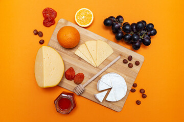 Naklejka na ściany i meble Wooden board with different cheeses, oranges, nuts, dried apricots, grapes and honey.