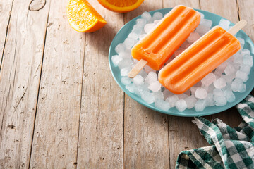 Orange popsicles on blue plate on rustic wooden table	.Copy space