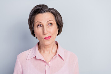 Photo of doubtful cute mature lady wear pink clothes smiling looking empty space isolated grey color background