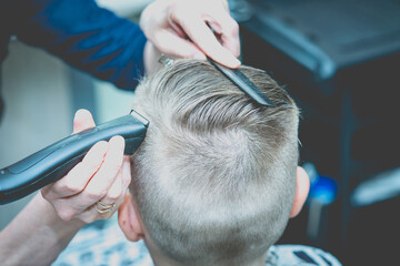 Hairdresser makes a fashionable pretty hairstyle for the young boy in a modern barbershop.Back view.Toned.Close-up.
