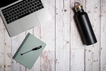 Laptop with notebook and pen and bottle of water for a home office or study on a weathered white wooden table background flat lay from above
