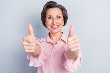 Photo of lucky cheerful age woman dressed pink shirt smiling showing two thumbs up isolated grey color background