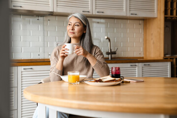 Mature grey woman drinking coffee while having breakfast