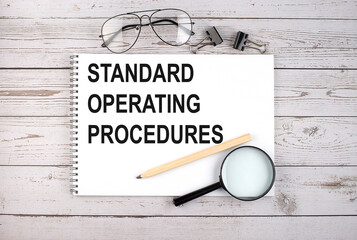 Notebook with text Standard Operating Procedure on the wooden table with pen, magnifier and glasses