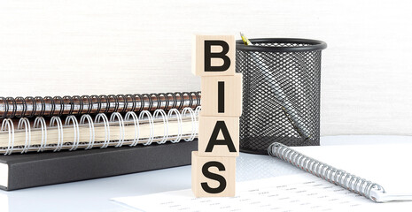 BIAS text on wooden block with notebooks on white background