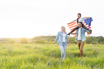 Patriotic holiday. Happy family, parents and daughters children girl with American flag outdoors....