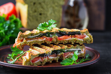 Vegetarian sandwich panini with spinach leaves, tomatoes and cheese on a dark table. Toast with cheese.