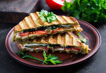 Vegetarian sandwich panini with spinach leaves, tomatoes and cheese on a dark table. Toast with cheese.