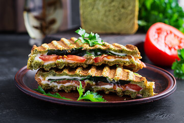 Vegetarian sandwich panini with spinach leaves, tomatoes and cheese on a dark table. Toast with cheese.
