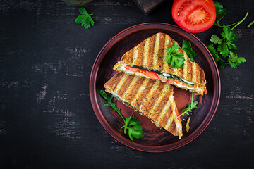 Vegetarian sandwich panini with spinach leaves, tomatoes and cheese on a dark table. Toast with cheese. Top view, overhead, copy space