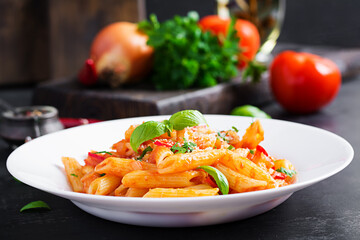 Classic italian pasta penne alla arrabiata with basil and freshly grated parmesan cheese on dark table. Penne pasta with chili sauce arrabbiata.