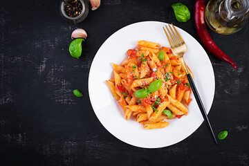 Classic italian pasta penne alla arrabiata with basil and freshly grated parmesan cheese on dark table. Penne pasta with chili sauce arrabbiata. Top view, above, copy space