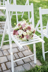 Wedding decoration. bridal bouquet on a white wooden chair. Guest area in the garden. Sunny day
