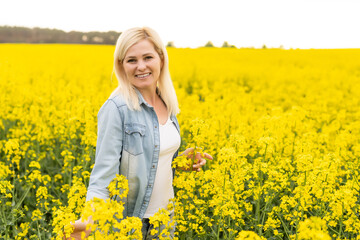 Naklejka na ściany i meble Portrait of attractive woman on blooming rapeseed field with sunset light. Yellow flowers and happy woman