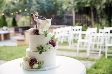 Wedding cake decorated with figures of the bride and groom and flowers. Wedding cake on the table outdoor. Selective focus.