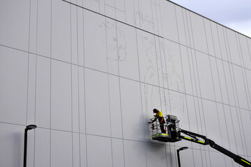 Australian artist using an articulated boom lift to creating a mural on a building exterior.Murals...