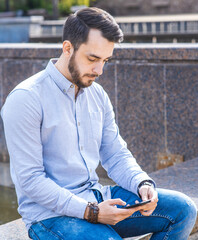 Obraz premium Portrait of a man businessman in a shirt with a beard who sits and uses a smartphone