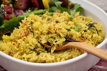 Yellow rice pilaf with wooden spoon, white dish