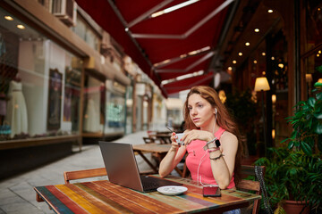 Young girl having tea in a coffee shop. Working with laptop and using a smartphone