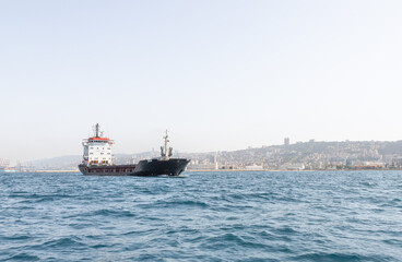 Fototapeta premium A large cargo ship is in the roadstead in the water area of the Haifa Bay, against the background of Haifa city, in the Mediterranean Sea, near the port of Haifa in Israel