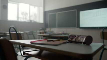 Notebook, pens and pencil case on desk in classroom. School supplies on table