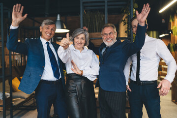 Happy group of colleagues standing in workplace with raised hands