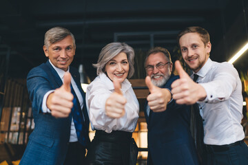 Smiling group of colleagues standing in workplace with thumbs up