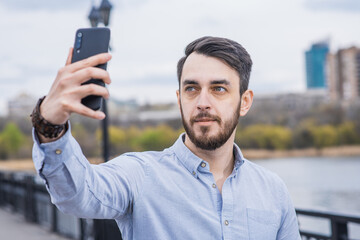 Portrait of a man businessman with a beard in a shirt who takes a selfie on a smartphone