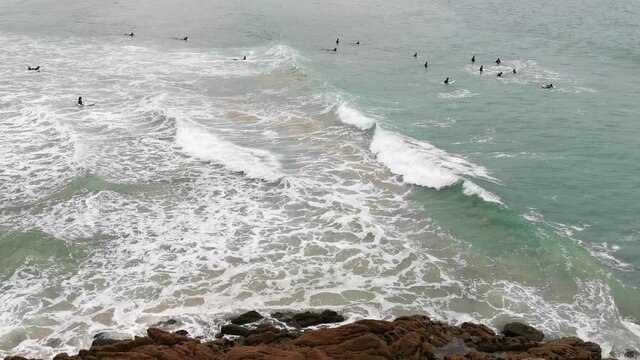 Alumnos de escuela de surf haciendo pr&aacute;cticas en las olas que llegan a la costa, visto desde arriba