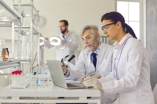 Scientists in protective goggles working in laboratory together. Senior male researcher and young female lab technician with sample test tube glass doing medical research and using laptop computer