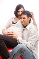 Fototapeta premium Portrait of Playful Caucasian Couple with Pregnant Wife Sitting Embraced Over White Background.