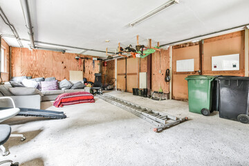Garbage bins and various furniture placed inside spacious garage with lumber walls in house