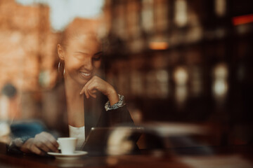 woman in a coffee shop drink coffee viewed through glass with reflections as they sit at a table chatting and laughing