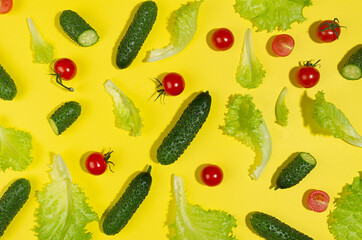 Food colorful vegetables pattern - cherry tomatoes, green gherkin cucumber, salad leaves in hard light with shadow on yellow background, flat lay.