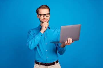 Photo of young man serious confident hand touch chin think look laptop project report isolated over blue color background