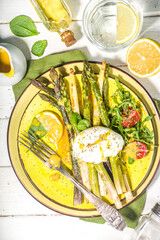 Healthy food, baked grilled asparagus, poached egg and hollandaise sauce on white wooden background copy space top view