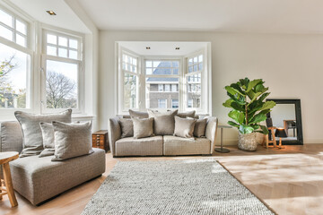 Fototapeta na wymiar Spacious light living room with large windows and white walls furnished with cozy sofa and armchair placed around carpet in modern apartment