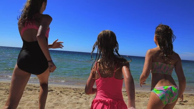 Three children having fun on a beach running to the sea slow motion
