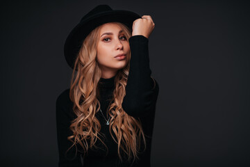 Portrait of a young beautiful woman in black hat on black background