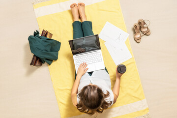 Businesswoman freelancer in office suit drinking coffee sitting  on beach towel of sand beach and working on laptop with graphics and charts. lunch break. Aerial view