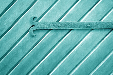 Old metal door hinge on wooden door in cyan tone.