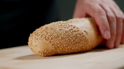 Human Hand holds A Crispy Baguette On cutting Board