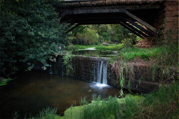 Small man-made waterfall under old bridge