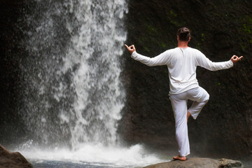 Man standing in meditation yoga on rock at waterfall