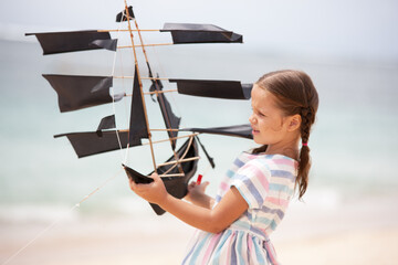 Girl playing on beach flying ship kite. Child enjoying summer.