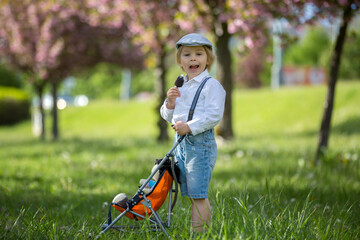 Fashion toddler child, eating ice cream and pushing kids stroller with knitted doll in it