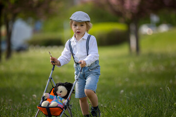 Fashion toddler child, eating ice cream and pushing kids stroller with knitted doll in it